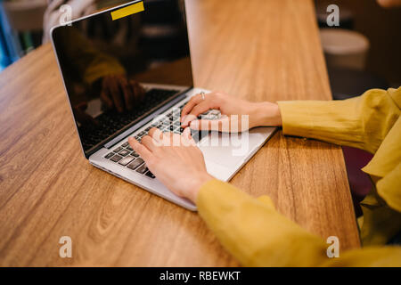 Eine junge Malay asiatische Frau, ist das Schreiben und Arbeiten oder Studieren auf Ihren Laptop in einem Cafe während des Tages. Sie trägt einen Turban Hijab. Stockfoto