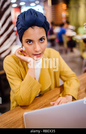 Eine junge Malay asiatische Frau, ist das Schreiben und Arbeiten oder Studieren auf Ihren Laptop in einem Cafe während des Tages. Sie trägt einen Turban Hijab. Stockfoto