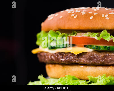 Frische leckere gegrillte Burger auf schwarzen Hintergrund. Fleisch Patty, Tomaten, Gurken, Kopfsalat und Sesam. Fast food Junk Food lifestyle Konzept. Stockfoto