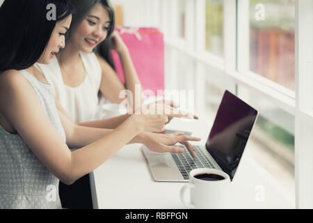 Zwei asiatische Frau zusammen Einkaufen mit Tüten in der Hand und mit Laptop, Shopping online Konzept. Stockfoto