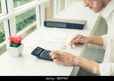 Asiatische Geschäftsmann mit einem Taschenrechner die Zahlen auf seinem Schreibtisch zu berechnen. Buchhalter Berechnung der Finanzen. Stockfoto