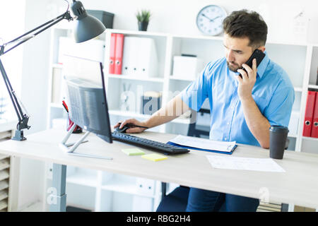 Ein junger Mann, der im Büro am Computer und am Telefon zu sprechen. Stockfoto