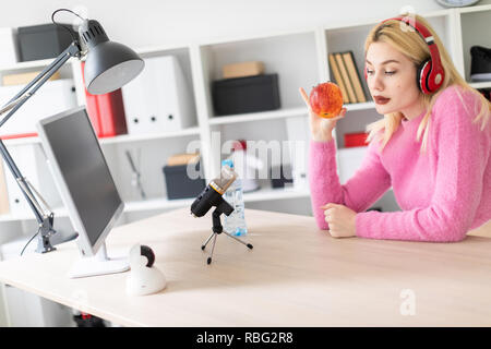 Ein junges Mädchen mit Kopfhörern am Tisch sitzen und mit einem Apfel. Stand vor ihr Mikrofon. Stockfoto