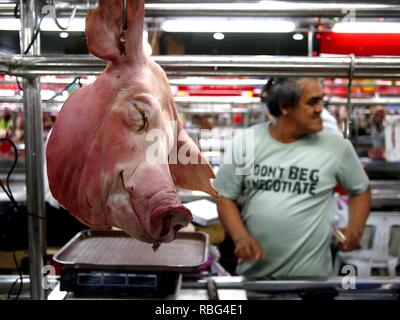 PASIG CITY, Philippinen - Dezember 23, 2018: ein Metzger in einer Fleisch Abschnitt von einem öffentlichen Markt und ein schweinekopf auf Anzeige an seinem Stall. Stockfoto