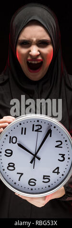 Porträt der schönen schweren Angst junge muslimische Frau mit schwarzen Hijab halten Sie clock in ihre Hände als Laufzeit Konzept auf schwarzem Hintergrund Angst Stockfoto