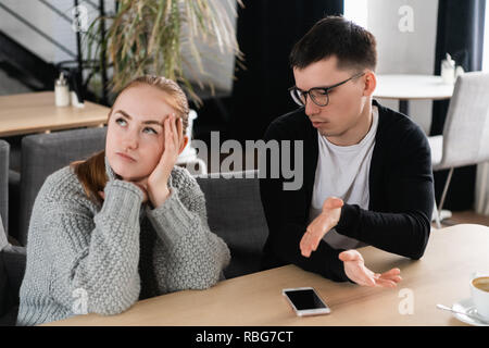 Verärgert man versuchen, etwas zu seiner Frau sitzt auf einer Couch im Cafe zu erklären Stockfoto