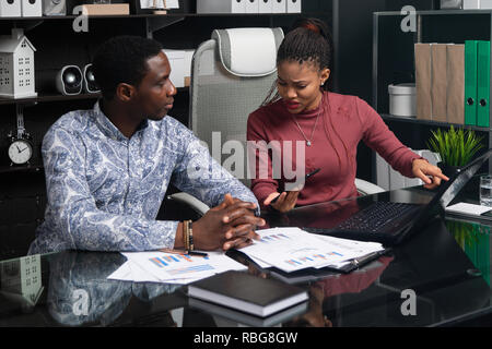 Die jungen Menschen der afroamerikanischen Nationalität Arbeiten mit Dokumenten und Telefon am Tisch im Büro Stockfoto