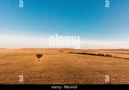 Hot Air Balloon Schatten auf dem Boden bei Sonnenaufgang über das Tal fliegen Stockfoto