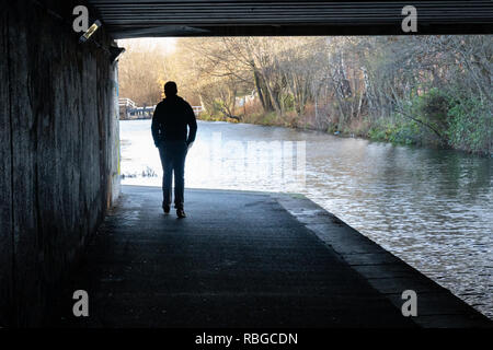 Silhouette eines Mannes, der lässig unter einem Viadukt auf dem Leeds und Liverpool Canal, West Yorkshire, England, Großbritannien, läuft. Stockfoto