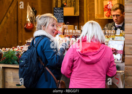 Mann bei Abschaltdruck arbeiten Verkauf von alkoholischen Fruchtliköre und potentielle Kunden (Frauen Kumpel) genießen Sie Drinks - York Weihnachtsmarkt, England, UK. Stockfoto