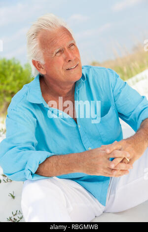 Portrait Of Happy attraktiv aussehenden älteren Mann draußen sitzen auf einem Strand nachdenklich Stockfoto