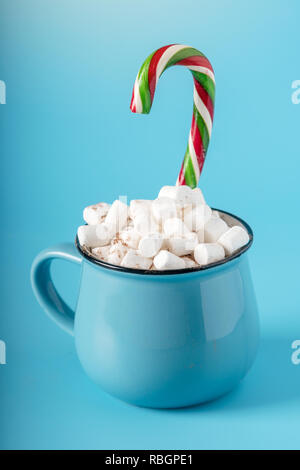 Tasse heiße Schokolade mit Marshmallows auf und halten einen Lutscher auf einem blauen Hintergrund. Gemütliche warme Winter Karte Stockfoto