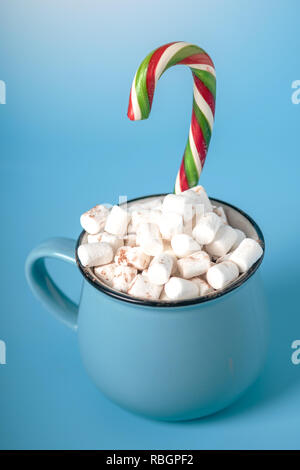 Tasse heiße Schokolade mit Marshmallows auf und halten einen Lutscher auf einem blauen Hintergrund. Gemütliche warme Winter Karte Stockfoto