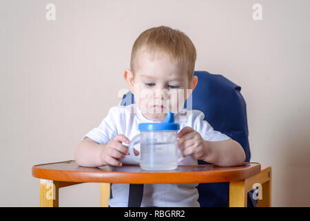 Little baby boy Trinkwasser Studium eine Plastikflasche beim Sitzen auf einem Stuhl in der Küche. Stockfoto