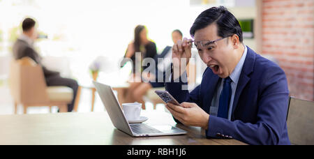 Portrait von Asiatische Geschäftsmann feiern und froh für seinen Erfolg im Cafe mit Smartphone und Laptop mit Business Team im Hintergrund für copor Stockfoto
