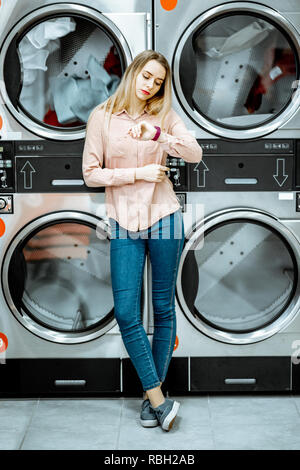 Junge Frau, die in der Nähe des Trockners Maschinen für Kleidung in der Self Service Wäsche getrocknet werden, warten Stockfoto