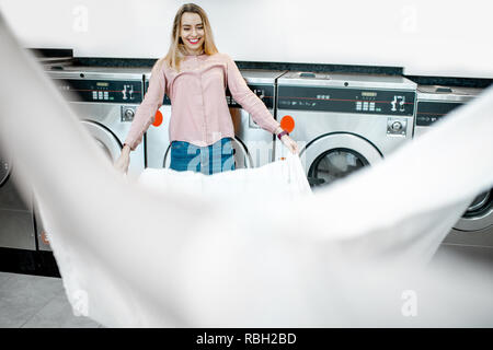 Junge Frau oben werfen ein Bettlaken, Kleidung nach dem Waschen in die öffentliche Wäscherei Stockfoto