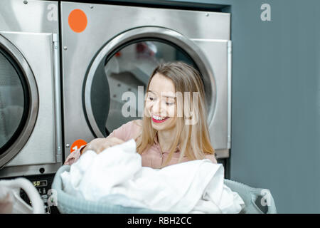 Porträt eines fröhliche Frau mit sauberem und getrocknete Kleidung in der Wäscherei Stockfoto