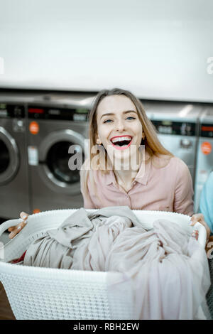 Portrait von eine fröhliche Frau, die mit Körben voller Kleider für die Wäsche in der Waschküche Stockfoto