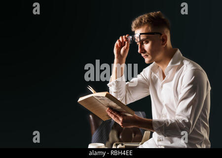 Buchen Sie Schriftsteller Brille und weißem T-Shirt auf dem Tisch mit Schreibmaschine und Lesen neues Buch Stockfoto