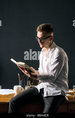 Buchen Sie Schriftsteller Brille und weißem T-Shirt auf dem Tisch mit Schreibmaschine und Lesen neue interessante Buch Stockfoto