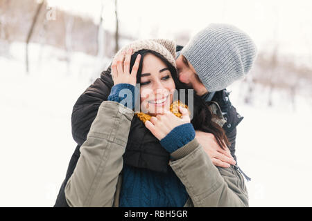 Glückliches junges Paar beim Winterurlaub Lächeln und Umarmungen auf einer unscharfen Winter Landschaft Hintergrund. Stockfoto