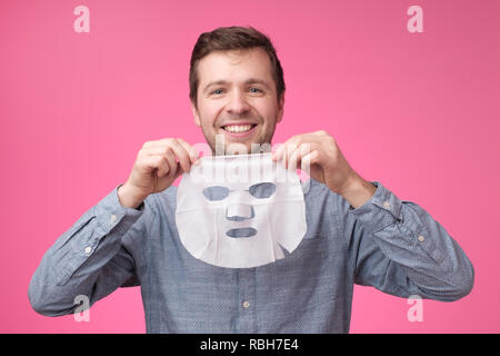 Junge europäische Mann in Gesichtsmaske auf rosa Hintergrund. Pflege selbst, dabei darauf achten, dass über seine Haut Stockfoto
