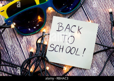 Zerstreut Beleuchtete winzige LED Stringlight auf Holz- Oberfläche. Zwei bunte Sonnenbrille mit Licht widerspiegelt. Handgeschriebene Nachricht zurück erinnern an Schoolt Stockfoto