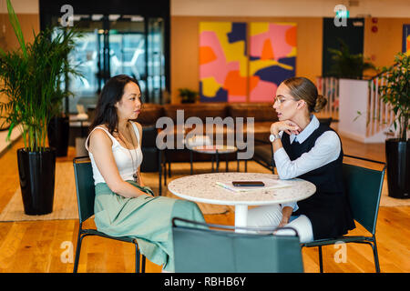 Zwei junge Frauen haben ein Treffen zusammen in einem Büro während des Tages. Sie werden von einem Team, ist Kaukasisch, die anderen Chinesischen. Stockfoto