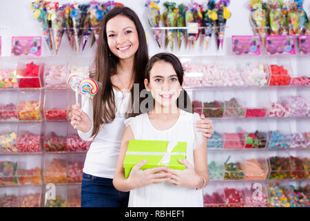 Lächelnde Frau mit Tochter holding Süßigkeiten und Geschenke in Candy shop Stockfoto