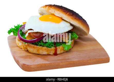 Appetitlich Cheeseburger mit gegrilltem Rindfleisch Patty, Spiegelei, Speck in Scheiben schneiden und frischem Gemüse. Auf weissem Hintergrund Stockfoto