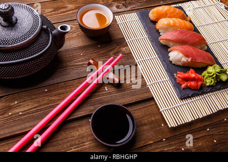 Sushi Set serviert auf grauem Stein Schiefer mit Sojasoße, grau Teekanne und Tasse Tee Stockfoto