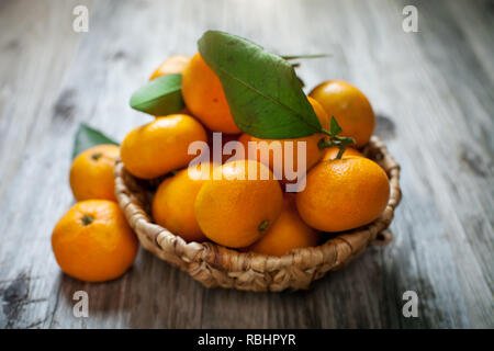 Mandarinen mit Blättern in Korb auf rustikalen Holzmöbeln Hintergrund. Stockfoto