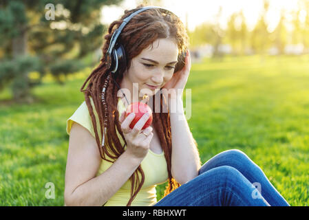 Schöne, moderne Frau Musik Hören mit Ihren Kopfhörern auf dem Hintergrund der Natur im Herbst sonnigen Park. Das Konzept der Melomania und gute Laune Stockfoto