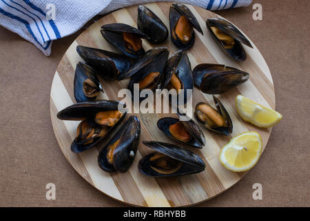 Köstliche gedämpfte Muscheln bereit, zusammen mit einer halben Zitrone auf einer Holzplatte zu essen. Ansicht von oben Stockfoto