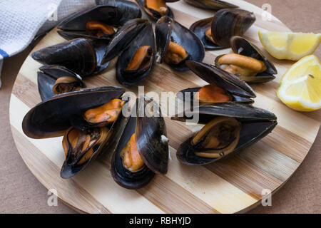Köstliche gedämpfte Muscheln bereit, zusammen mit einer halben Zitrone auf einer Holzplatte zu essen Stockfoto
