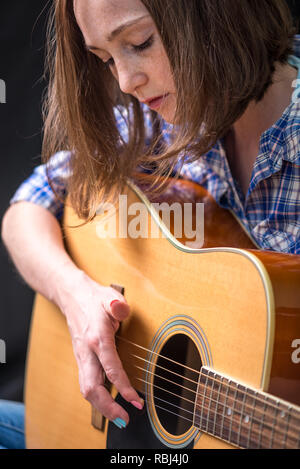 Das Mädchen Teenager spielen eine akustische Gitarre auf einem dunklen Hintergrund im Studio. Konzert junger Musiker Stockfoto