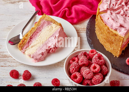 Nahaufnahme eines Teils einer White Chocolate Raspberry cheesecake auf einem Teller. geschnitten Käsekuchen auf einen schwarzen Stein Fach mit Stoff und gefrorene Himbeeren Stockfoto