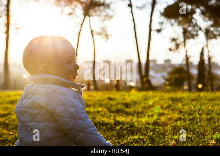 9 Monat Baby unter Sonnenstrahlen auf Gras Park. Vorteile des Sonnenlichts für Babys Konzept Stockfoto