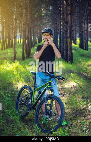 Man Radfahrer ist das Tragen eines Sport grau Helm auf seinem Kopf im Hintergrund der grüne Natur. Das Konzept der obligatorischen Schutz beim Radfahren Stockfoto