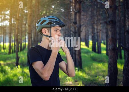 Man Radfahrer ist das Tragen eines Sport grau Helm auf seinem Kopf im Hintergrund der grüne Natur. Das Konzept der obligatorischen Schutz beim Radfahren Stockfoto
