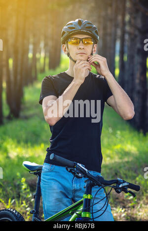 Man Radfahrer ist das Tragen eines Sport grau Helm auf seinem Kopf im Hintergrund der grüne Natur. Das Konzept der obligatorischen Schutz beim Radfahren Stockfoto