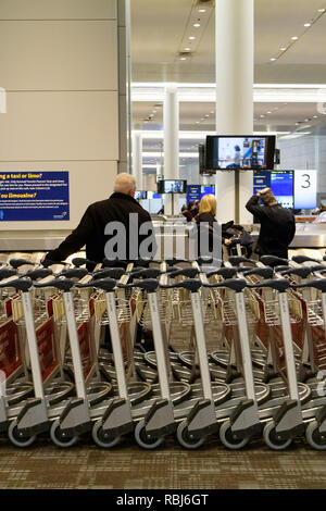 Menschen, die durch die Reihen der Gepäckwagen in Toronto Pearson Flughafen warten auf Ihrem Gepäck ankommen. Stockfoto