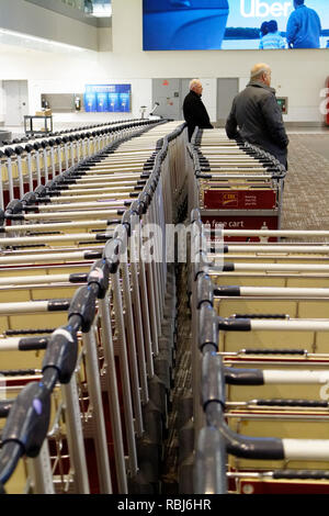 Menschen, die durch die Reihen der Gepäckwagen in Toronto Pearson Flughafen warten auf Ihrem Gepäck ankommen. Stockfoto