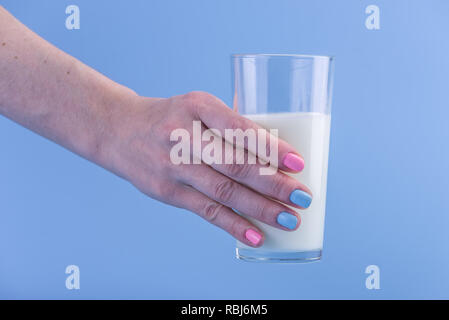 Die Hand einer Frau hält ein Glas frische Milch vor einem blauen Hintergrund. Bunte Minimalismus. Das Konzept der gesunde Milchprodukte mit Kalzium Stockfoto