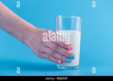 Die Hand einer Frau hält ein Glas frische Milch vor einem blauen Hintergrund. Bunte Minimalismus. Das Konzept der gesunde Milchprodukte mit Kalzium Stockfoto