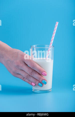 Die Hand einer Frau hält ein Glas frische Milch mit einem Strohhalm auf blauem Hintergrund. Bunte Minimalismus. Das Konzept der gesunde Milchprodukte mit Kalzium Stockfoto