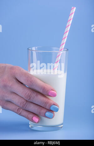 Die Hand einer Frau hält ein Glas frische Milch mit einem Strohhalm auf blauem Hintergrund. Bunte Minimalismus. Das Konzept der gesunde Milchprodukte mit Kalzium Stockfoto