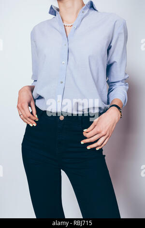 Modisch, elegante junge Frau in Schwarz Skinny Jeans, blaues Hemd und Perlenkette auf weißem Hintergrund gekleidet. Stockfoto