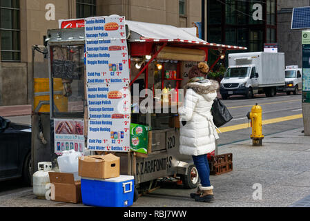 Eine Frau kauft ein Würstchen aus einem Street Food Verkäufer in Toronto, Kanada Stockfoto